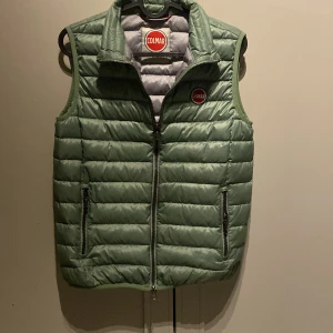 Grön dunväst från Colmar - Snygg ljusgrön dunväst från Colmar med quiltad design och dragkedja framtill. Västen har två fickor med dragkedja.Klassisk Colmar-logga på bröstet. Perfekt att slänga under en hoodie eller tröja för extra värme. Köpt för en månad sedan och sparsamt använd.