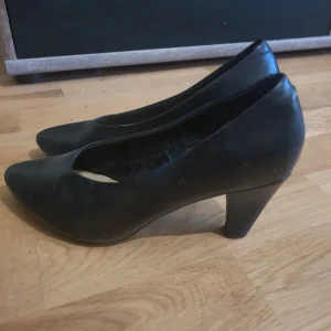 Svarta pumps från Alley - Klassiska svarta pumps från Alley med spetsig tå och medelhög klack. Skorna är tillverkade i syntetmaterial och har en stilren design som passar till många olika outfits.