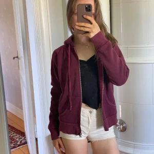 Vinröd hoodie med dragkedja från Gina Tricot - Mysig vinröd hoodie från Gina Tricot med dragkedja, huva och broderad detalj på bröstet. Används inte så tänkte att någon annan kanske vill ha den mer :))