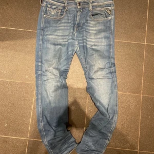 Blå Replay Hyperflex Anbass jeans - Säljer ett par blå Replay Hyperflex Anbass jeans med klassisk femficksdesign och dragkedjegylf. Jeansen har en något tvättad look och raka ben. Perfekta för dig som gillar bekväma och stilrena jeans.