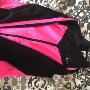 Nike svart och rosa tröja XL - Nike tröja i svart och starkt rosa med dragkedja framtill. Sportig design med det klassiska Nike-logga på bröstet. Tröjan har lång ärm och är rätt så varm. 