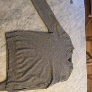 Grå kashmirtröja från J.Crew - Mjuk och stilren grå tröja i italiensk kashmir från J.Crew. Klassisk rund halsringning och ribbade muddar vid ärmslut och nederkant. Perfekt för lager-på-lager och en tidlös bas i garderoben. litet hål på armen men de går att fixa. Skriv innan ni köper. Pris kan diskuteras