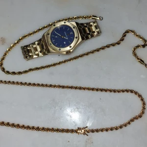 Guldfärgad klocka med blå urtavla och cordell - Stilren guldfärgad klocka med blå urtavla och metallarmband. Klockan har en rund boett med markerade skruvar och tydliga indexmarkeringar. Passar dig som gillar klassisk design med en modern touch.