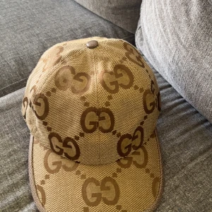 Beige keps från Gucci med GG-mönster - Snygg beige keps från Gucci med det klassiska GG-mönstret i brunt. Justerbar rem baktill och insida i ljus bomull. Perfekt accessoar för en trendig look. Helt ny fick den för 1 vecka sen 