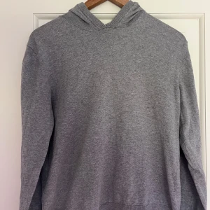 Grå stickad hoodie  - Säljer en enkel och stilren grå hoodie från Grunt. Tröjan är tillverkad i mjuk bomull, har lång ärm och huva. Perfekt för dig som gillar en clean och avslappnad look. Passar till det mesta och är superbekväm att bära.