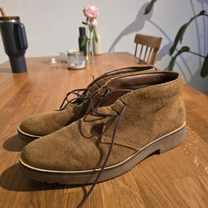 Ljusbruna mockaboots från Timberland - Säljer ett par klassiska bruna mockaboots från Timberland med snörning och rund tå. Skorna har platt sula och är perfekta för höst och vinter. Tidlös design med Timberland-logga på sidan och bekväm innersula.