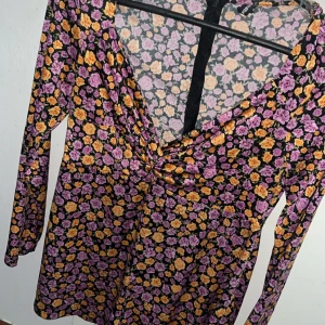 Blommig långärmad jumpsuit  - Säljer en långärmad jumpsuit med  tätt blommönster i lila och gult. Klänningen har v-ringning och lätt twistad detalj framtill. Perfekt för dig som gillar färg och mönster!