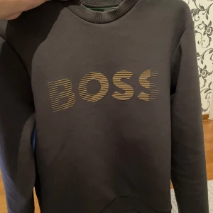Svart sweatshirt från BOSS - Säljer en svart sweatshirt från BOSS med guldfärgad logotyp framtill. Tröjan har rund halsringning och långa ärmar. Perfekt för en stilren och avslappnad look. Köpt för 1599kr förra året! Men säljer nu för 499kr