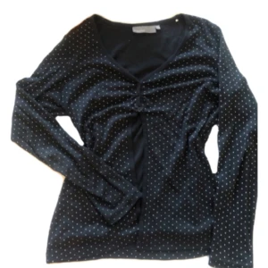 Svart prickig långärmad topp - Svart långärmad topp med små vita prickar och v-ringning. Snygg detalj med rynkning framtill som ger en cool look. Perfekt att styla med jeans eller kjol för en trendig outfit.
