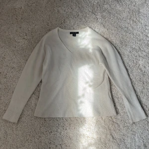 Vit stickad v-ringad tröja Amisu - Vit stickad tröja från Amisu med v-ringning och långa ärmar. Tröjan har breda ribbade muddar vid ärmslut och nederkant, vilket ger en snygg och enkel look. Perfekt för lager-på-lager under kyliga dagar.