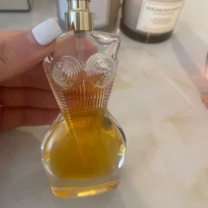 Jean Paul Gaultier Classique parfym - Ikonisk parfym i en genomskinlig glasflaska formad som en kvinnokropp med detaljerad byst och guldigt spruthuvud. Doften är varm och sensuell, och flaskan har en bärnstensfärgad vätska. Perfekt för dig som gillar unika och snygga flaskor.