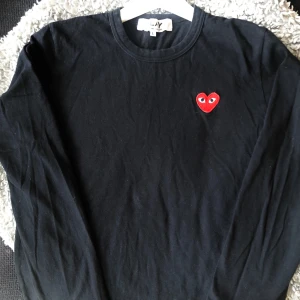 Svart långärmad tröja Comme des Garçons - Svart långärmad tröja från Comme des Garçons Play med det ikoniska röda hjärtat med ögon broderat på bröstet. Tillverkad i 100% bomull, rund halsringning och clean design som ger en stilren vibe.