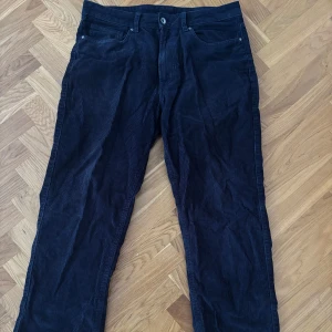 Mörkblå manchesterbyxor - Säljer ett par mörkblå manchesterbyxor med klassisk femficksdesign och raka ben. Byxorna har normal passform och stängs med knapp och dragkedja. Perfekta för dig som gillar en tidlös stil med lite retrovibe.