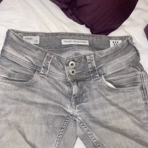 Grå bootcut jeans från Pepe Jeans - Snygga grå jeans från Pepe Jeans med bootcut passform och raka ben. Jeansen har dubbla knappar i midjan, klassiska fickor fram och bak samt coola slitningar nertill. Perfekta för dig som gillar en avslappnad men trendig look. Jeansen har 2 defekter en vid ett pyttelitet hål där nere som man ser på femte bilden sen har dom en fläck på bakbenet som jag skickar bild på vid frågan om det eftersom ja inte får plats med mer bilder. Midjemått är 35-36 rakt över och passar mig som är 160 be om mer bilde