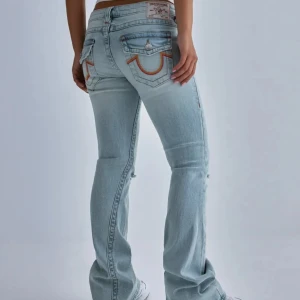 True Religion jeans - Säljer ett par ljusblå bootcut jeans från True Religion med slitningar på knäna och klassiska bakfickor med orange sömmar. Jeansen har låg midja och är i storlek 23. Knappt använda💞