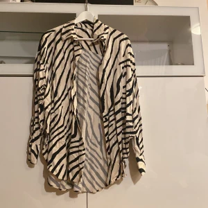 Zebramönstrad skjorta i vitt och svart - Säljer en snygg zebramönstrad skjorta i vitt och svart. Skjortan har lång ärm och en lös passform, perfekt för dig som vill sticka ut lite extra. Den är tillverkad i ett lätt material och har klassisk krage.