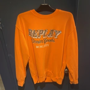 Orange sweatshirt från Replay - Säljer en orange sweatshirt från Replay med tryckt logga och texten 'Denim Goods' på bröstet. Tröjan har rund hals, långa ärmar och är tillverkad i mjuk bomull. Perfekt för dig som gillar färg och streetstyle. Använd max 3 gånger