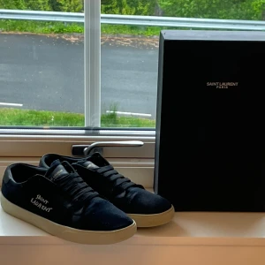 Svarta sneakers från Saint Laurent - Säljer ett par svarta Saint Laurent sneakers med vit sula och logga på sidan. Skorna har klassisk snörning och rund tå. Perfekta för dig som gillar stilrena och exklusiva sneakers. riktigt bra skick funkar 42 och 44 med 