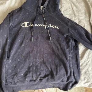 Mörkblå hoodie från Champion - Säljer en mörkblå hoodie från Champion med vit broderad logga framtill och små diskreta Champion-loggor över hela tröjan.