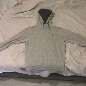 Grå hoodie från U.S. Polo Assn, M - Säljer en stilren grå hoodie från U.S. Polo Assn i storlek M och den kan passa som S .Tröjan har huva med svarta snören, känguruficka och diskret logga på bröstet. Perfekt för chill dagar och enkel att matcha med jeans eller joggers.