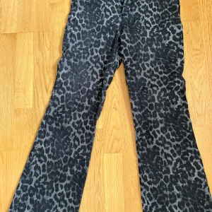 Svarta leopardmönstrade jeansbyxor - Säljer ett par svarta jeansbyxor med leopardmönster. Byxorna har normal passform och klassisk femficksdesign med knapp och dragkedja i midjan. Perfekta för dig som vill sticka ut med ett djuriskt mönster.
