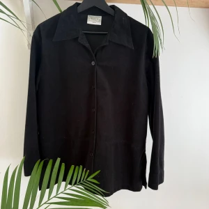 Svart skjorta, Rosetti -  svart skjorta från Rosetti, tyget är polyester men känns och ser ut som manchester/sammet. Klassisk krage, knäppning framtill och långa ärmar. Rak passform.