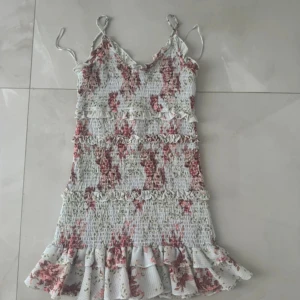 Blommig Zara klänning med volang - Supersöt klänning med blommigt mönster. Klänningen har smala axelband, volangdetaljer och smockad passform som ger en feminin siluett. Perfekt för sommaren