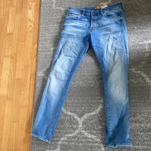 Slim fit jeans från Jack & Jones - Snygga ljusblå slim fit jeans från Jack & Jones, modell Glenn. Klassisk femficksdesign, lätt slitna detaljer och bekväm passform. Perfekta för dig som gillar en smalare siluett och vill ha ett par stilrena jeans i bomull.