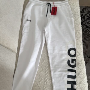 Vita mjukisbyxor från HUGO BOSS - Snygga vita mjukisbyxor från HUGO med stor svart logga längs ena benet och mindre logga framtill.  Byxorna är i helt nytt skick och helt oanvända. Byxorna är fel köpta. Nypris: 1399