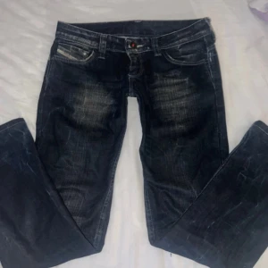 Ultra low waist Mörkblå jeansbyxor från Diesel - Säljer ett par mörkblå jeans från Diesel med slitna detaljer och kontrastsömmar. Klassisk femficksmodell med knappgylf och tydlig Diesel Industry-logga på fickan. Snygg tvätt och raka ben.