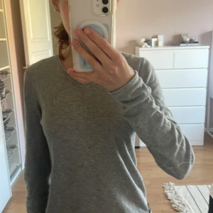 Grå långärmad tröja från Harcour - Säljer en stilren grå långärmad tröja från Harcour med v-ringning. Tröjan har broderad logga på bröstet och stor brodyr på ryggen💞