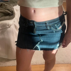 Mörkblå Disel jeanskjol❣️ - Säljer en mörkblå jeanskjol med rå kant och slitna detaljer. Den har en sönder grej se på bilden ovan. Skriv om ni vill ha bilder eller har frågor att ställa❣️storleken är oklar jag hittar inget som visar men som referens är jag 167, jag kan även skicka midjans längd om någon är intresserad 🥰