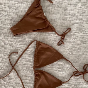 Bikini från Aqua tropic - Snygg brun bikini med trekantsöverdel och knytband i sidorna. Perfekt för soliga dagar på stranden. Enkel och stilren design som ger en naturlig look. Från märket Aqua Tropic. Trosan storlek M och toppen M.