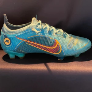 Nike Mercurial vapor elite - Snygga Nike Mercurial fotbollsskor i blått med gula och röda detaljer. Skorna har snörning, låg profil och mönstrad sula för bra grepp på planen. Tillverkade i syntetmaterial med cool design och tydlig Nike-logga på sidan.