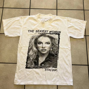 Vit t-shirt med tryck - Cool vit t-shirt med ett stort tryck av en känd artist och texten 'The Sexiest Woman'. Perfekt för fans som vill ha en unik stil. Längd 61 cm, bröstomkrets 98 cm