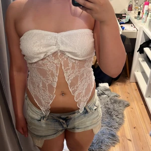 Vit spets topp - Supersöt vit topp i spets. Toppen är axelbandslös och har en unik, öppen design nertill. Perfekt för dig som vill sticka ut med en feminin och trendig look.