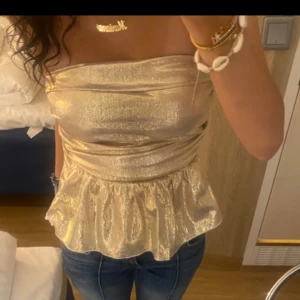 Glud tubtopp med volang - Guld topp. Den är omsydd så den sitter tajtare men skulle ändå säga den är storlek xs