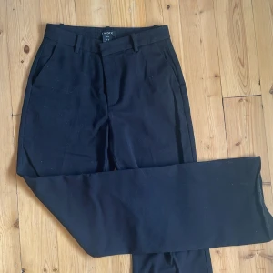 Svarta kostymbyxor från Lindex - Klassiska svarta kostymbyxor från Lindex, modell Fiona. Byxorna har raka ben, hällor för bälte, snedställda fickor fram och en diskret bakficka. Perfekta för en clean och stilren look. Materialet är mjukt och känns bekvämt hela dagen. Lite slitna längst ner, därav priset😊❤️