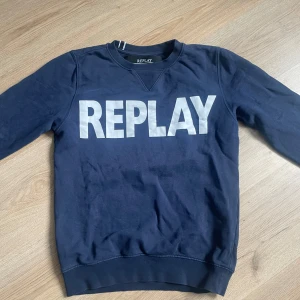 Marinblå sweatshirt från Replay - Snygg marinblå sweatshirt från Replay med stort vitt tryck över bröstet. Tröjan har rund hals, långa ärmar och ribbade muddar vid ärmslut och nederkant. Perfekt för dig som gillar streetwear och vill ha en enkel men stilren look.