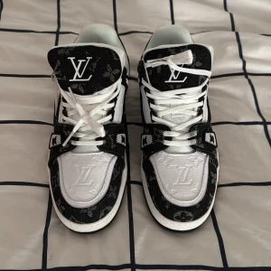 Louis Vuitton svartvita sneakers - Obs: har inte använt dem och dem är riktiga. Snygga Louis Vuitton sneakers i svart och vitt med klassiskt LV-monogram på tygdetaljerna. Skorna har vit läderbas, svarta kontraster och tydlig logga på plösen och sulan. Platt sula, rund tå och vita snören ger en clean och lyxig vibe.