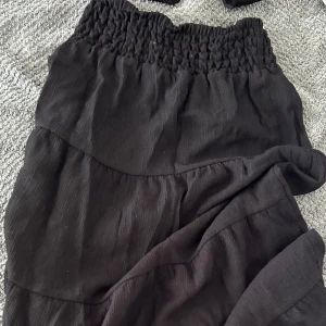 Svart långkjol från H&M med volang - Svart långkjol från H&M med bred, smockad midja och volangdetaljer. Kjolen har en mjuk, lätt struktur och är perfekt för dig som gillar en enkel men snygg look. Passar dig som vill ha en flowy och bekväm kjol till garderoben. Pris går såklart att diskutera! 🖤