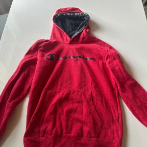 Röd Champion hoodie X-Large - Säljer en röd hoodie från Champion i storlek X-Large. Tröjan har svart foder i huvan, klassisk Champion-logga broderad på bröstet och en stor magficka framtill. Perfekt för chill dagar och streetwear-stil.