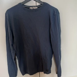 Blå långärmad tröja från H&M - En basic blå långärmad tröja från H&M i mjuk bomull. Tröjan har rund halsringning och ribbade muddar vid ärmslut och nederkant. Perfekt för lager-på-lager och enkel att matcha med jeans eller chinos.