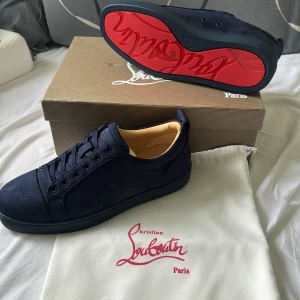 Mörkblå sneakers från Christian Louboutin - Helt nya och oanvända! Snygga mörkblå sneakers från Christian Louboutin i mocka med ikonisk röd sula och broderad logga på hälen. Skorna har rund tå, snörning och beige innersula med guldfärgad logotyp. Perfekt för dig som vill sticka ut med exklusiv stil.