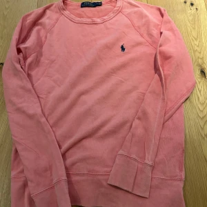 Rosa tröja från Polo Ralph Lauren - Säljer en chill rosa långärmad tröja från Polo Ralph Lauren i mjuk bomull. Klassisk rund hals och den ikoniska lilla blå Polo-loggan på bröstet. Perfekt för dig som gillar enkel och stilren design med en poppig färg.