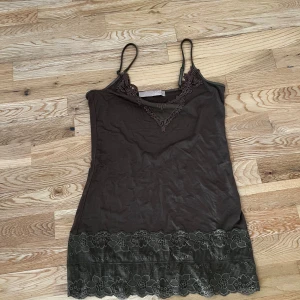 Linnetopp med spetsdetaljer från Culture - Supersøt lintopp fra Culture med smale stropper og v-hals dekorert med brodert blonde. Finnes i tre farger: brun, hvit og svart. Nederst er det en bred blondekant med blomstermønster. Kan sende hvis kjøperen betaler frakt💗