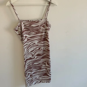 Brun och vit zebra klänning  - Säljer en kort klänning från storlek S med smala axelband. Klänningen har ett coolt zebramönster i brunt och vitt och är figurnära. Materialet är mjukt och lätt, perfekt för varma dagar. Supersnygg att styla med chunky sneakers eller boots. Bodycon