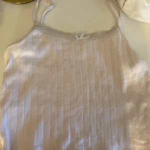 Söt ljusrosa ribbad linnetopp med spets - Ljusrosa linnetopp med smala axelband, ribbad struktur och diskret spetskant upptill. En liten rosett framtill ger extra gullig vibe. Perfekt för layering eller sommarhäng. Materialet känns mjukt och stretchigt. Jag står inte för packet försvinner i frakten,  35 kr + frakt