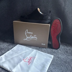 Svarta sneakers från Christian Louboutin - Snygga svarta sneakers från Christian Louboutin med klassisk röd sula och diskret logga på hälen. Skorna har rund tå, snörning och är tillverkade i mocka med läderfoder. Perfekt för dig som gillar exklusiv och stilren design med en lyxig touch.
