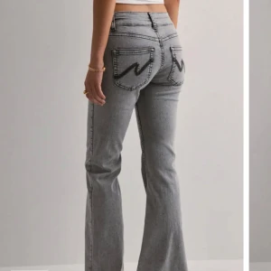 Grå bootcut jeans  - Säljer ett par grå bootcut jeans med snyggt svart broderi på bakfickorna. Jeansen har medelhög midja, klassisk femficksdesign och är tillverkade i mjukt denimtyg. Perfekta för dig som gillar en retro vibe och vill ha ett par jeans som sticker ut.